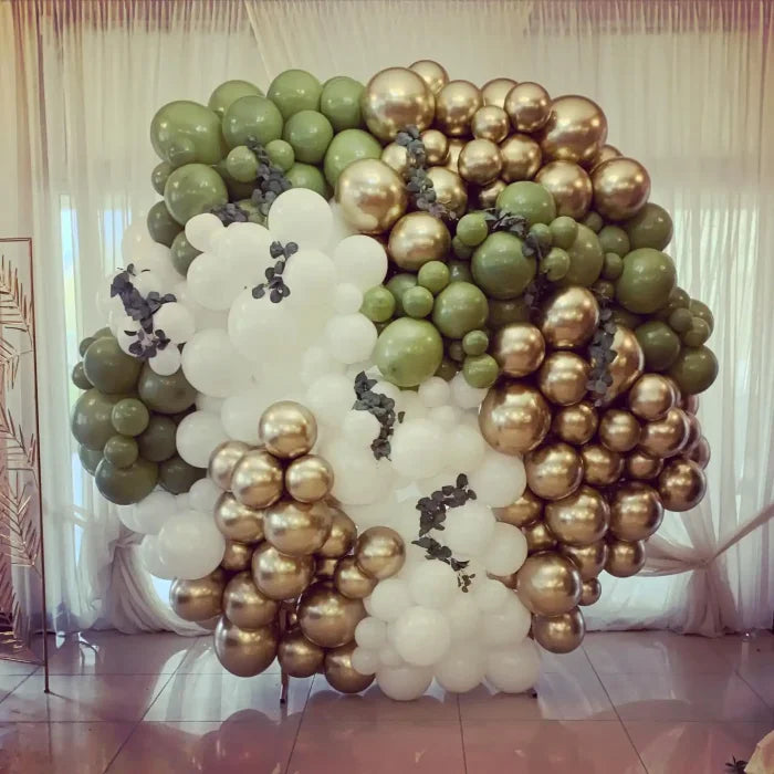 Łuk balonowy wykonany z białych, oliwkowych i chromowanych złotych balonów ułożonych w organiczny wzór.