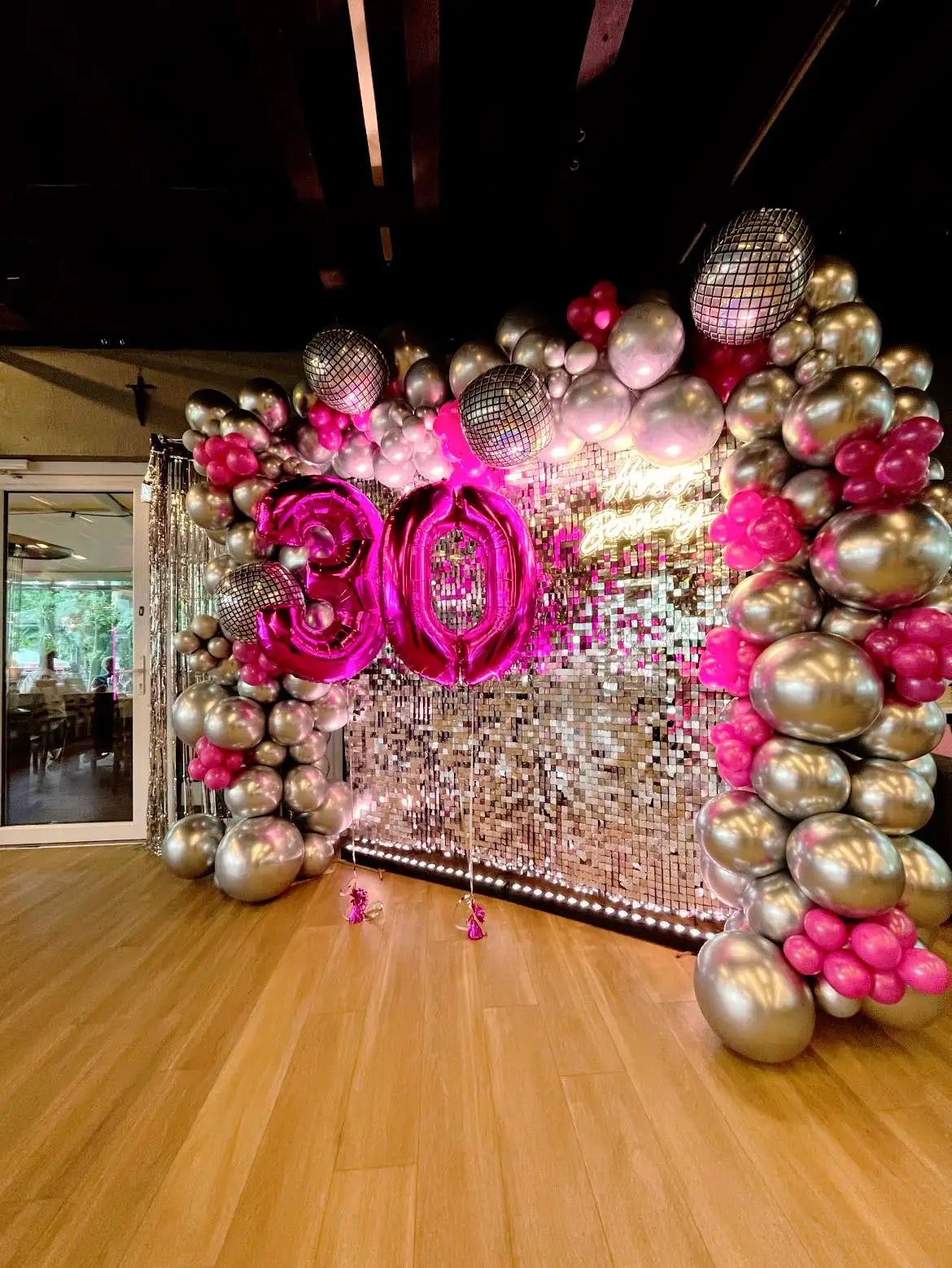 Błyszczący łuk balonowy w odcieniach różowego i srebrnego z akcentami w kształcie refleksyjnych kulek dyskotekowych.