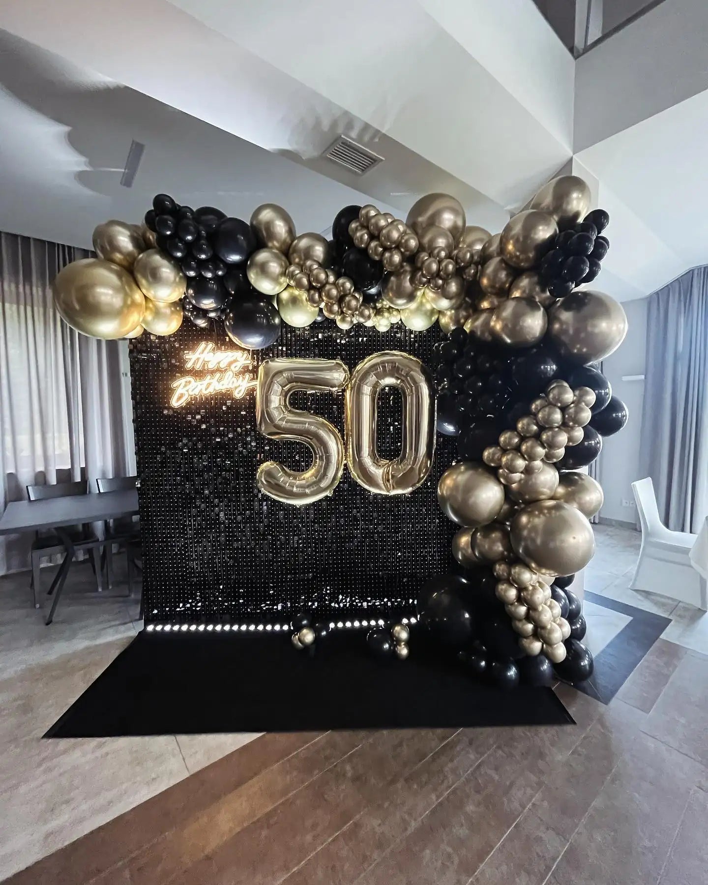 Czarna i złota łuk balonowy z błyszczącym tłem z cekinów, na którym znajdują się podświetlone balony ’50’’.