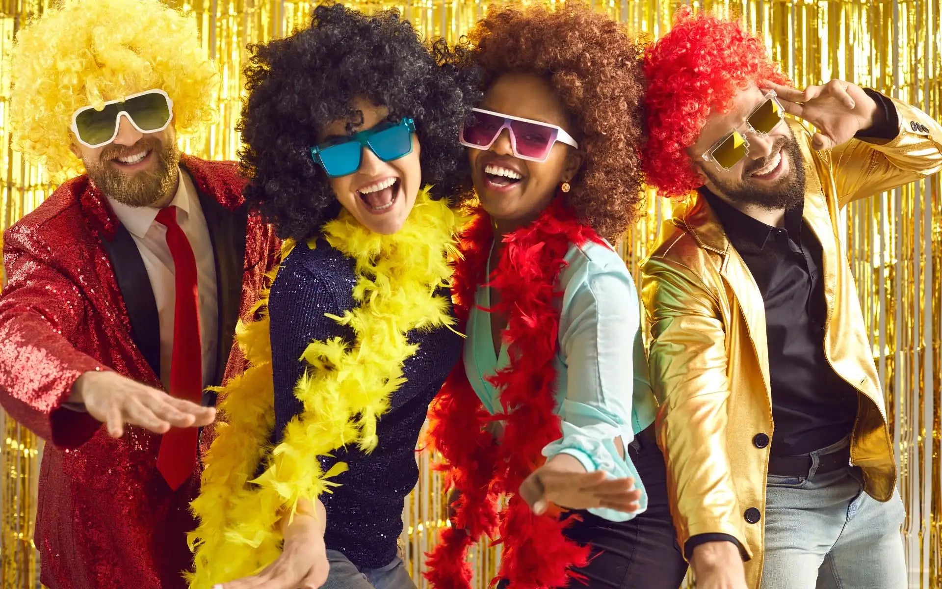 Cztery osoby w żywych, błyszczących kostiumach z kolorowymi perukami i okularami przeciwsłonecznymi pozują energicznie na tle złotego folii.