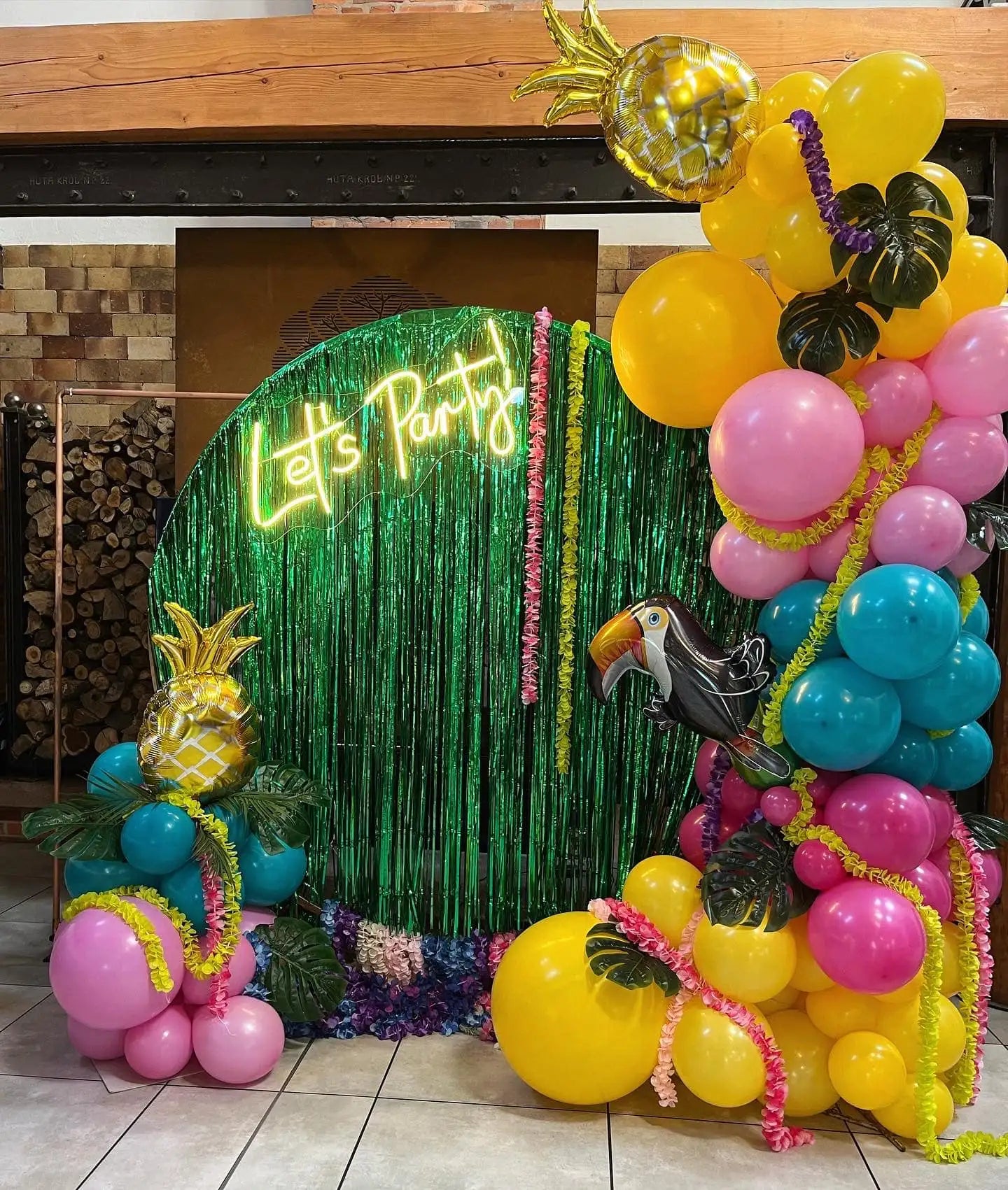 Tropikalny łuk balonowy z żywymi żółtymi, różowymi i niebieskimi balonami ozdobionymi złotymi foliowymi ananasami i wycięciami czarnych tukana.