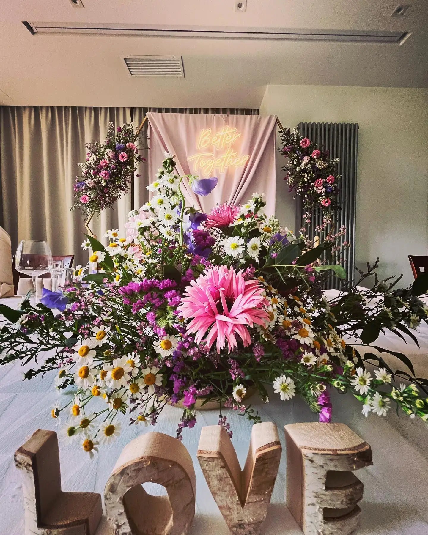 Wibrująca aranżacja mieszanych kwiatów w rustykalnej drewnianej wazie z różowymi stokrotkami i fioletowymi kwiatami.