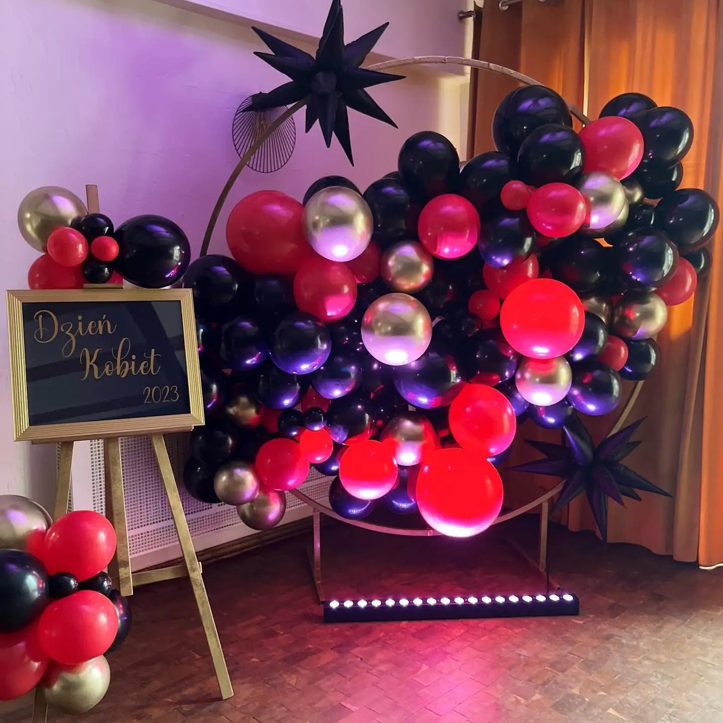 Wibrujący, w kształcie serca łuk balonowy złożony z błyszczących czarnych, promiennych czerwonych, lśniących złotych i głębokich fioletowych balonów.